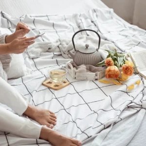 Frau liegt entspannt im Bett mit Handy und Tee Frau liegt entspannt im Bett mit Handy und Tee